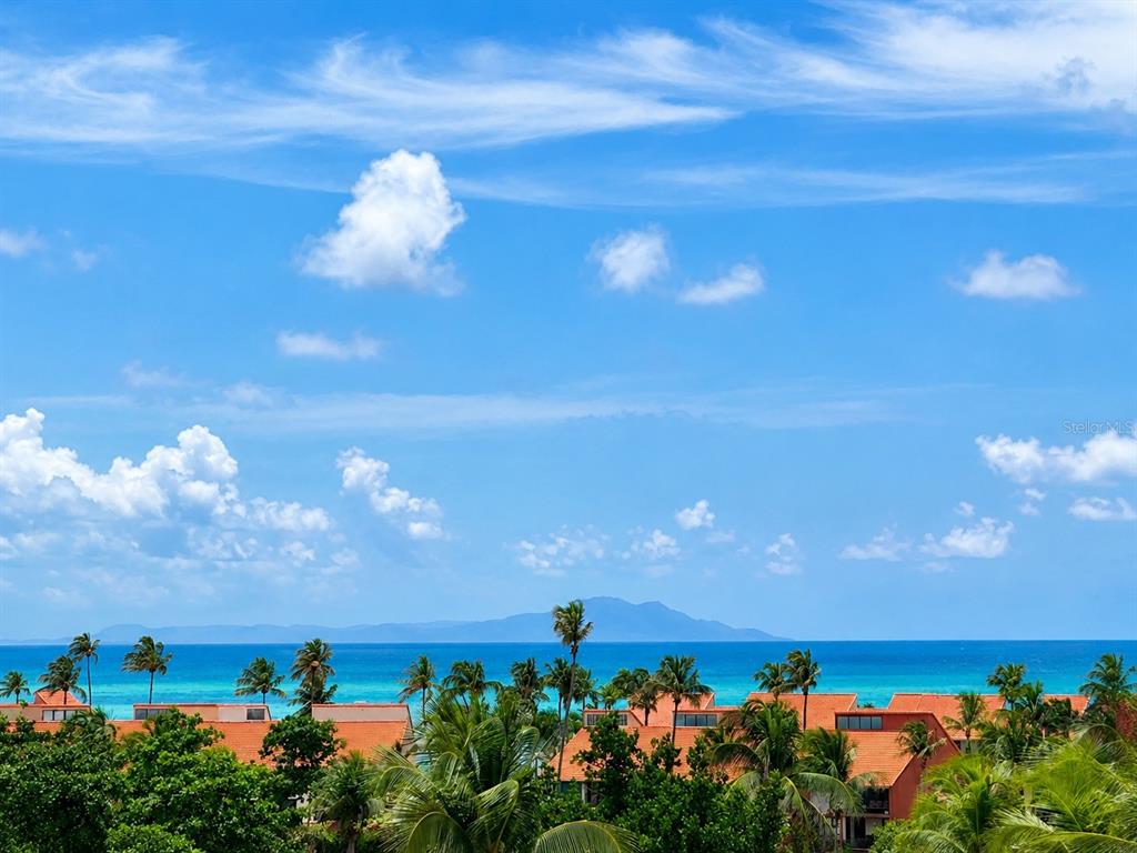 An exterior view of a tropical resort with palm trees, orange roofs, and ocean views — 285 PALMAS INN RD, PALMAS DEL MAR, UNIT 5102, HUMACAO, PR