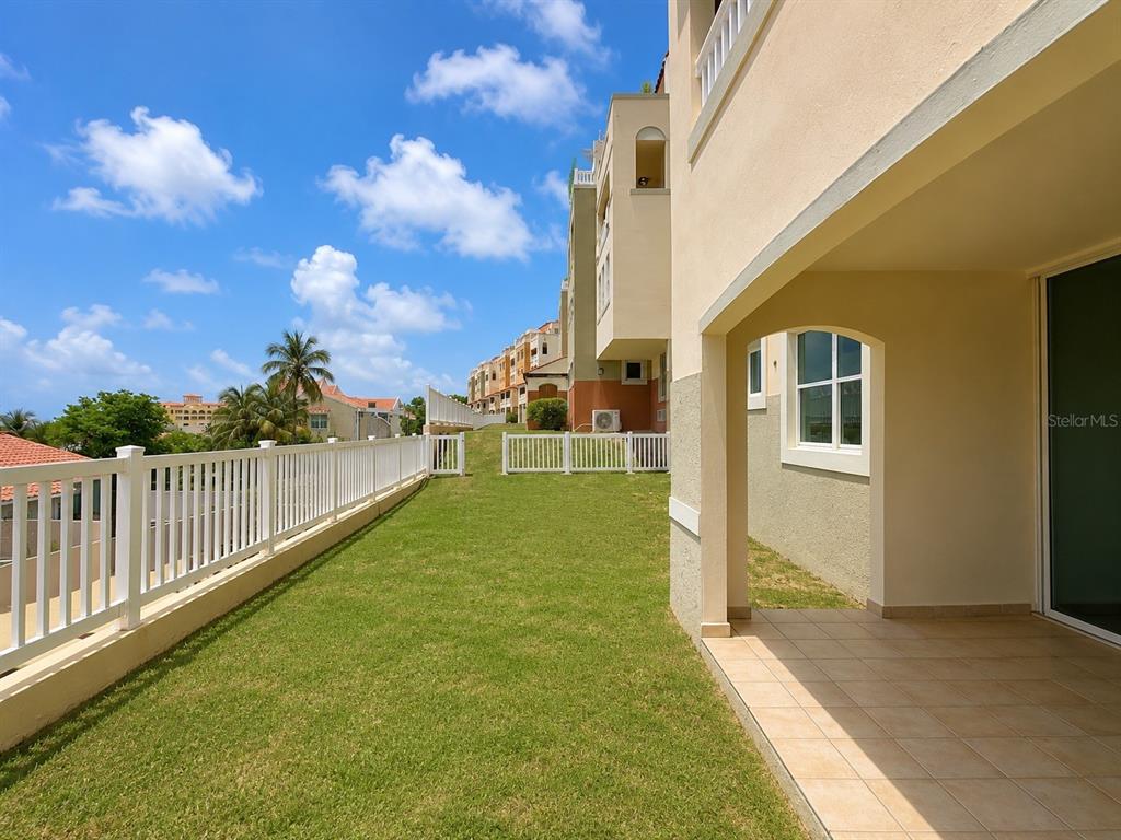A grassy backyard area with a white fence and a covered patio with tile flooring — 285 PALMAS INN RD, PALMAS DEL MAR, UNIT 5102, HUMACAO, PR