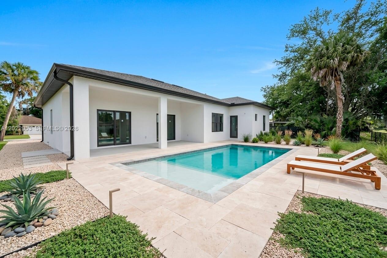 A modern white house exterior features a swimming pool, patio, and lounge chairs — 3286 EAGLE PASS ST, North Port FL 34286, NORTH PORT, FL