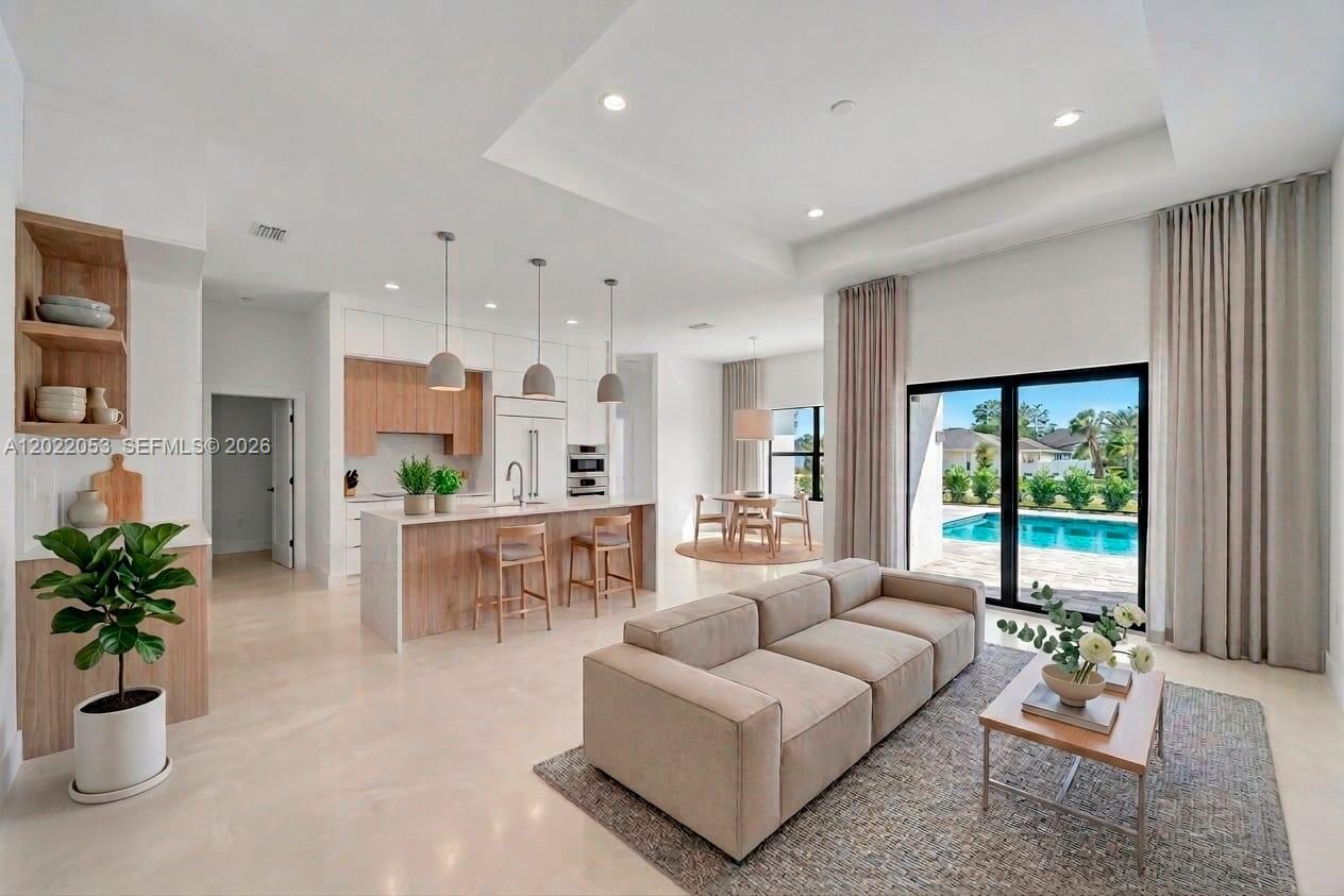 A modern open-concept living room and kitchen feature light wood cabinetry, tile floors, and pool views — 3286 EAGLE PASS ST, North Port FL 34286, NORTH PORT, FL