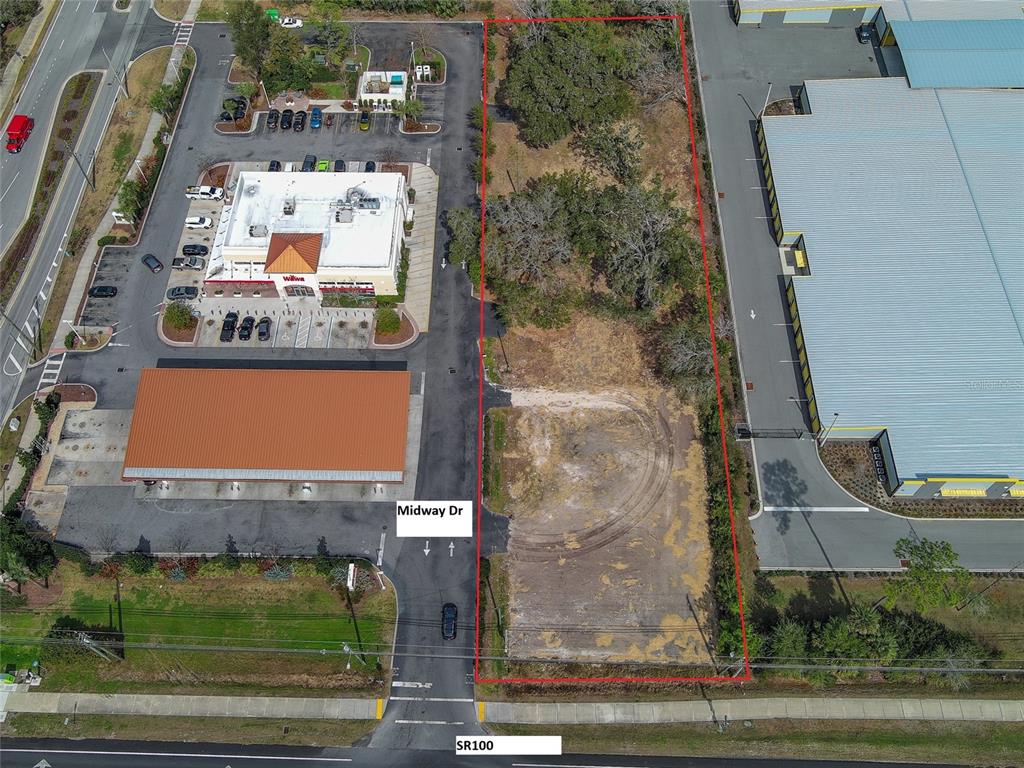 An aerial view shows a vacant, rectangular lot outlined in red next to commercial buildings — 2 MIDWAY DRIVE, PALM COAST, FL