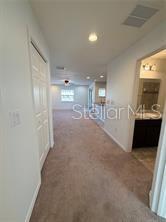 A carpeted hallway leads toward a bright living area with a view of the kitchen — 5051 CACTUS NEEDLE LANE, WESLEY CHAPEL, FL
