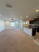 An open-concept living area features a kitchen with dark cabinets, an island, and carpeted flooring — 5051 CACTUS NEEDLE LANE, WESLEY CHAPEL, FL
