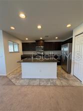 A kitchen features dark wood cabinets, a central island, stainless steel appliances, and tile flooring — 5051 CACTUS NEEDLE LANE, WESLEY CHAPEL, FL