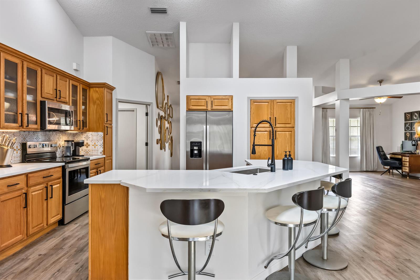 A kitchen with wood cabinets, stainless steel appliances, and a white quartz-topped island with stools — MELBOURNE, FL