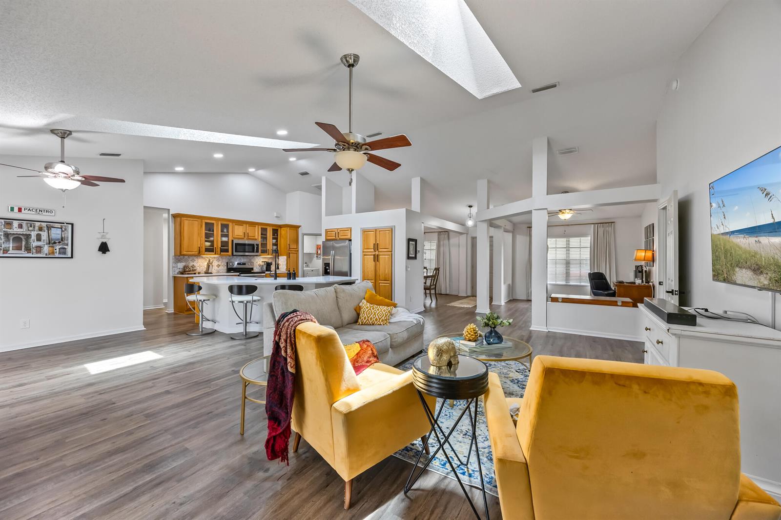 An open-concept living room and kitchen featuring vaulted ceilings, skylights, and wood-look flooring — MELBOURNE, FL