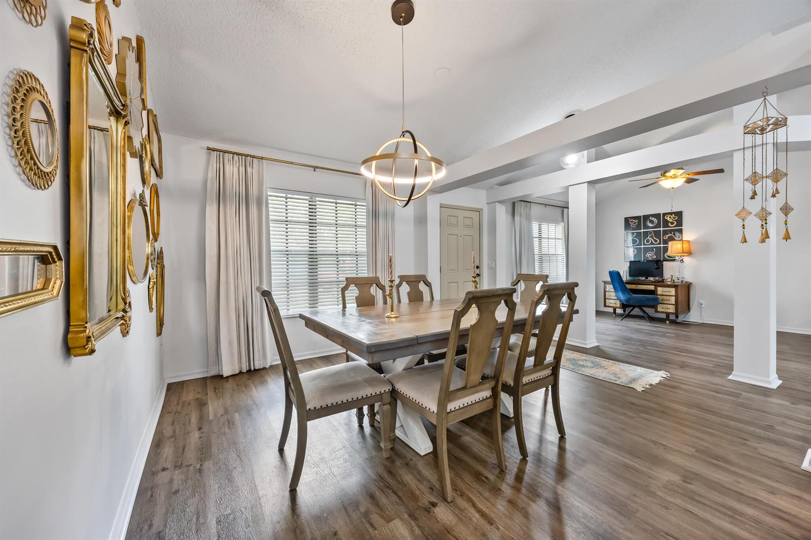 A dining room features a wooden table, upholstered chairs, a modern chandelier, and gold-framed mirrors — MELBOURNE, FL