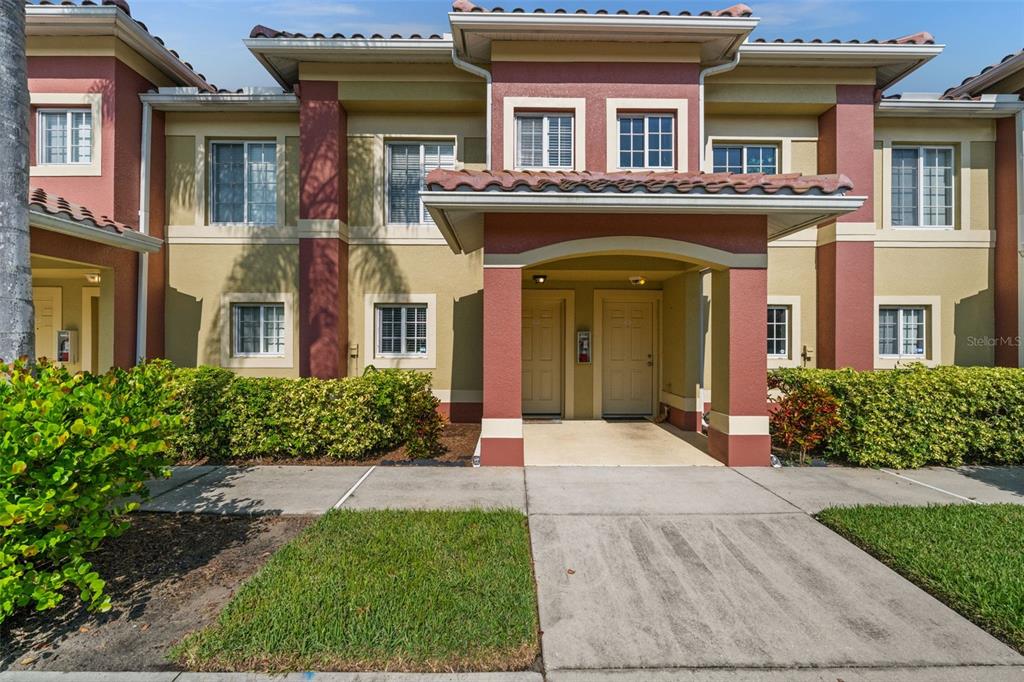 A two-story residential building exterior with a covered entryway, tan stucco walls, and red trim — 9430 IVY BROOK RUN UNIT 405, FORT MYERS, FL