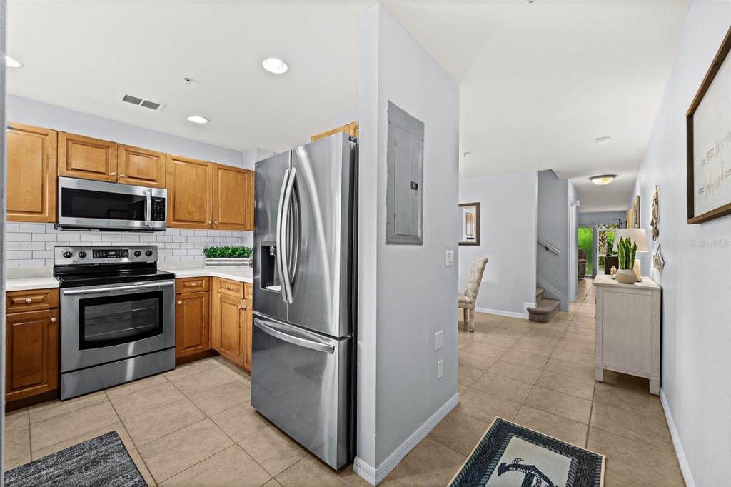 A kitchen with wood cabinets, stainless steel appliances, and tile flooring leads to a hallway — 9430 IVY BROOK RUN UNIT 405, FORT MYERS, FL