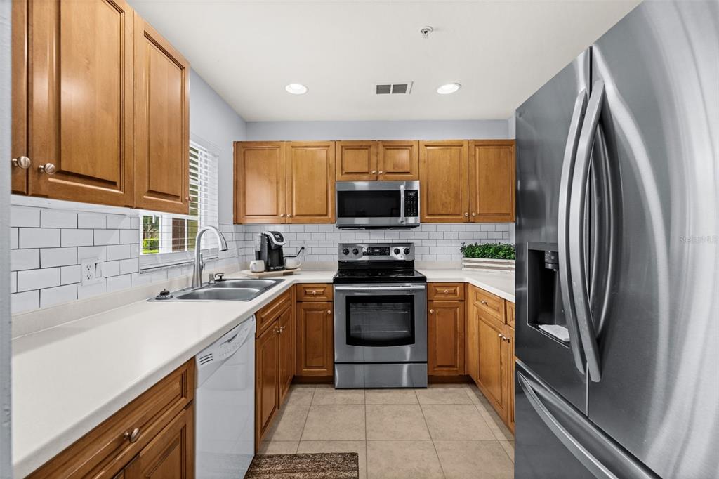 A kitchen with wooden cabinets, stainless steel appliances, white countertops, and a subway tile backsplash — 9430 IVY BROOK RUN UNIT 405, FORT MYERS, FL