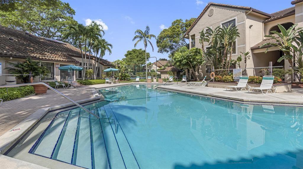 A swimming pool with lounge chairs and palm trees sits in front of apartment buildings — 4341 W Mcnab Road # 10, Pompano Beach FL 33069, POMPANO BEACH, FL
