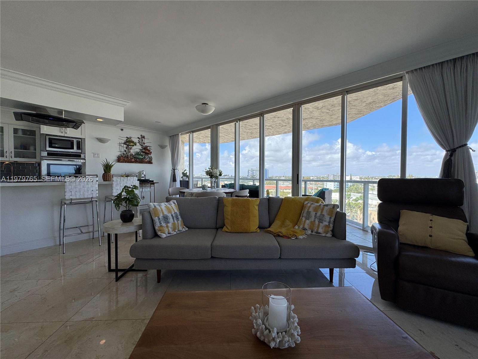 A living room features a gray sofa, a wooden coffee table, and floor-to-ceiling windows — 7330 Ocean Ter # D, Miami Beach FL 33141, MIAMI BEACH, FL