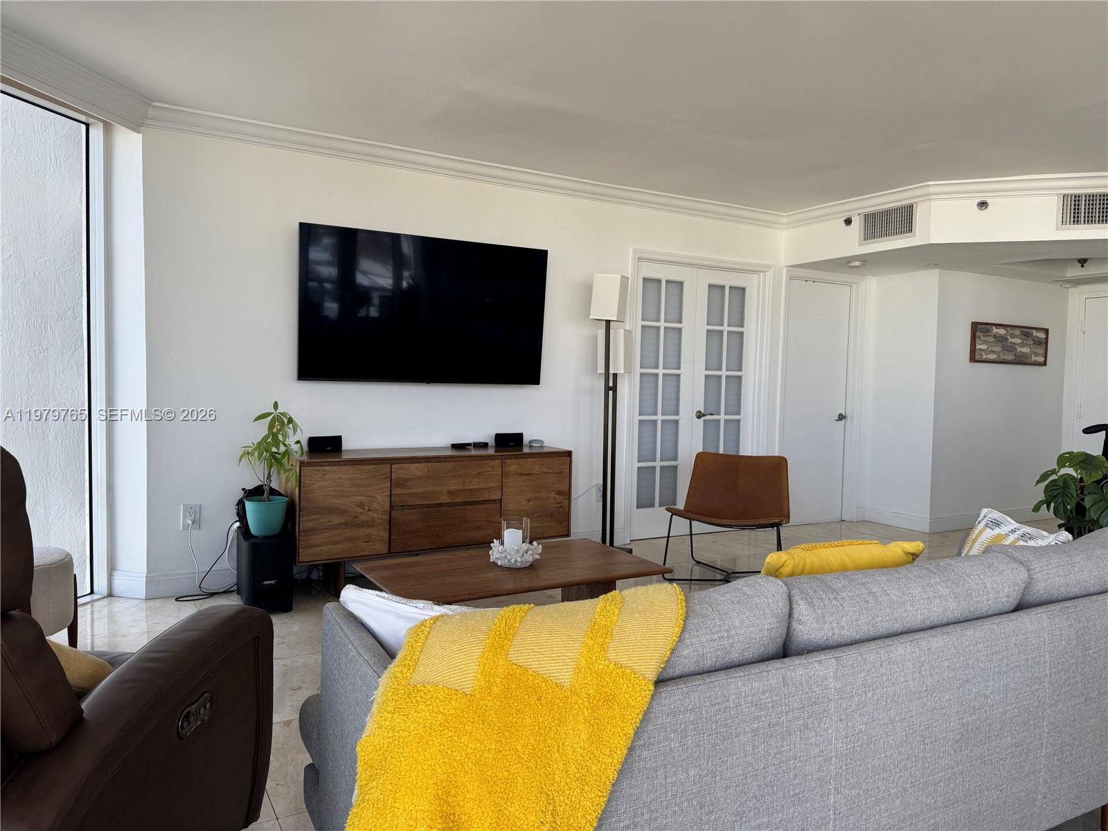 A living room features a wall-mounted television, a wooden media console, and gray seating — 7330 Ocean Ter # D, Miami Beach FL 33141, MIAMI BEACH, FL