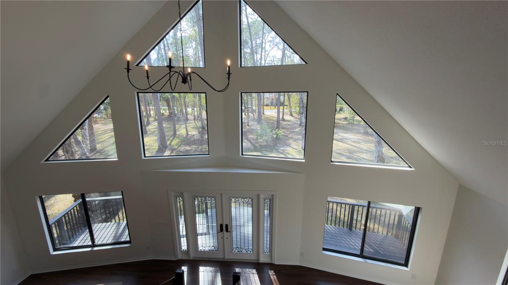 A high-ceilinged living room features large windows, a chandelier, and double glass doors — 8140 PIMLICO PLACE, WESLEY CHAPEL, FL