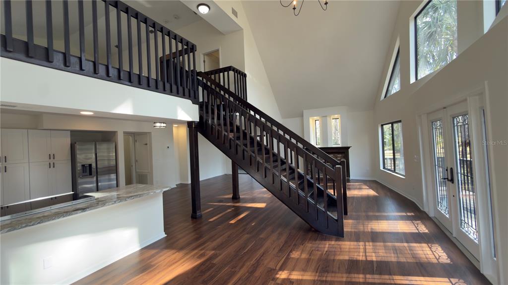 A spacious living area features a dark wood staircase, vaulted ceilings, and hardwood flooring — 8140 PIMLICO PLACE, WESLEY CHAPEL, FL