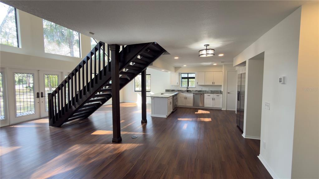 An open-concept living area features a dark wood staircase, white kitchen cabinetry, and wood flooring — 8140 PIMLICO PLACE, WESLEY CHAPEL, FL