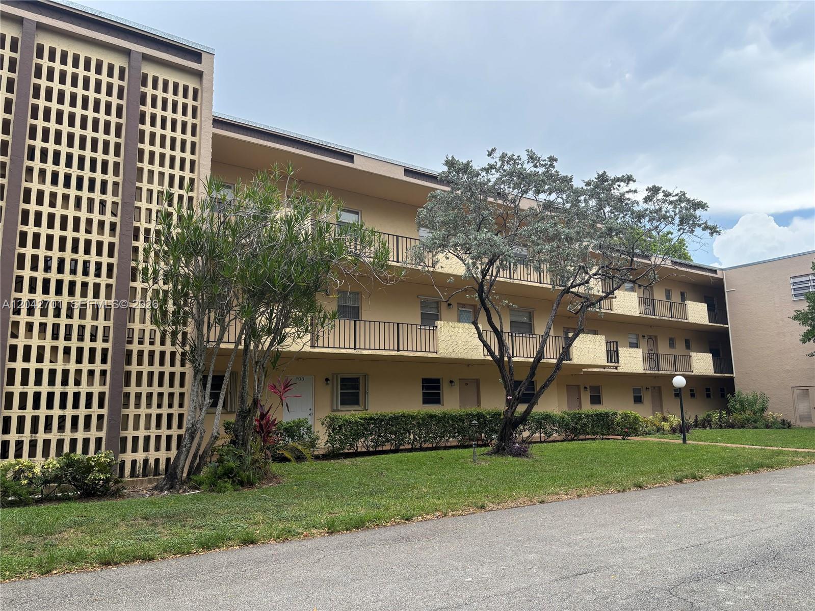 A three-story apartment building features beige stucco walls, black metal railings, and a decorative screen — 300 Berkley Rd # 103, Hollywood FL 33024, HOLLYWOOD, FL