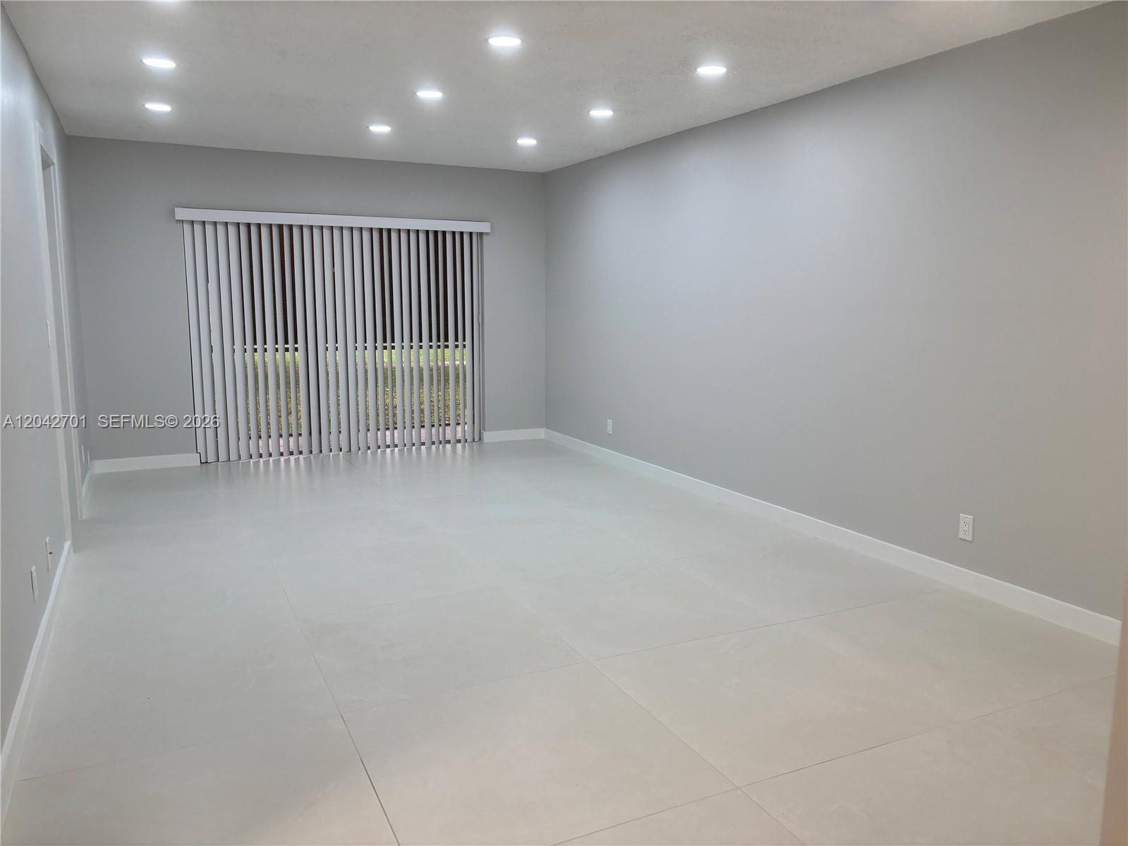 An empty room features light gray walls, large white floor tiles, and recessed ceiling lighting — 300 Berkley Rd # 103, Hollywood FL 33024, HOLLYWOOD, FL