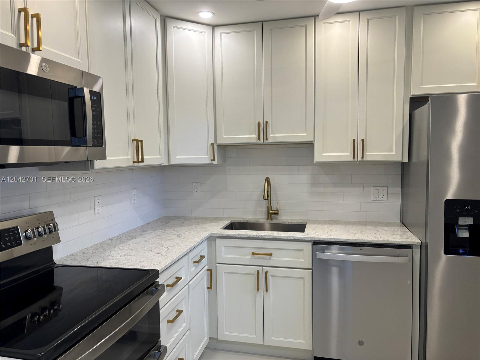 A kitchen features white cabinets, gold hardware, stainless steel appliances, and a quartz countertop — 300 Berkley Rd # 103, Hollywood FL 33024, HOLLYWOOD, FL