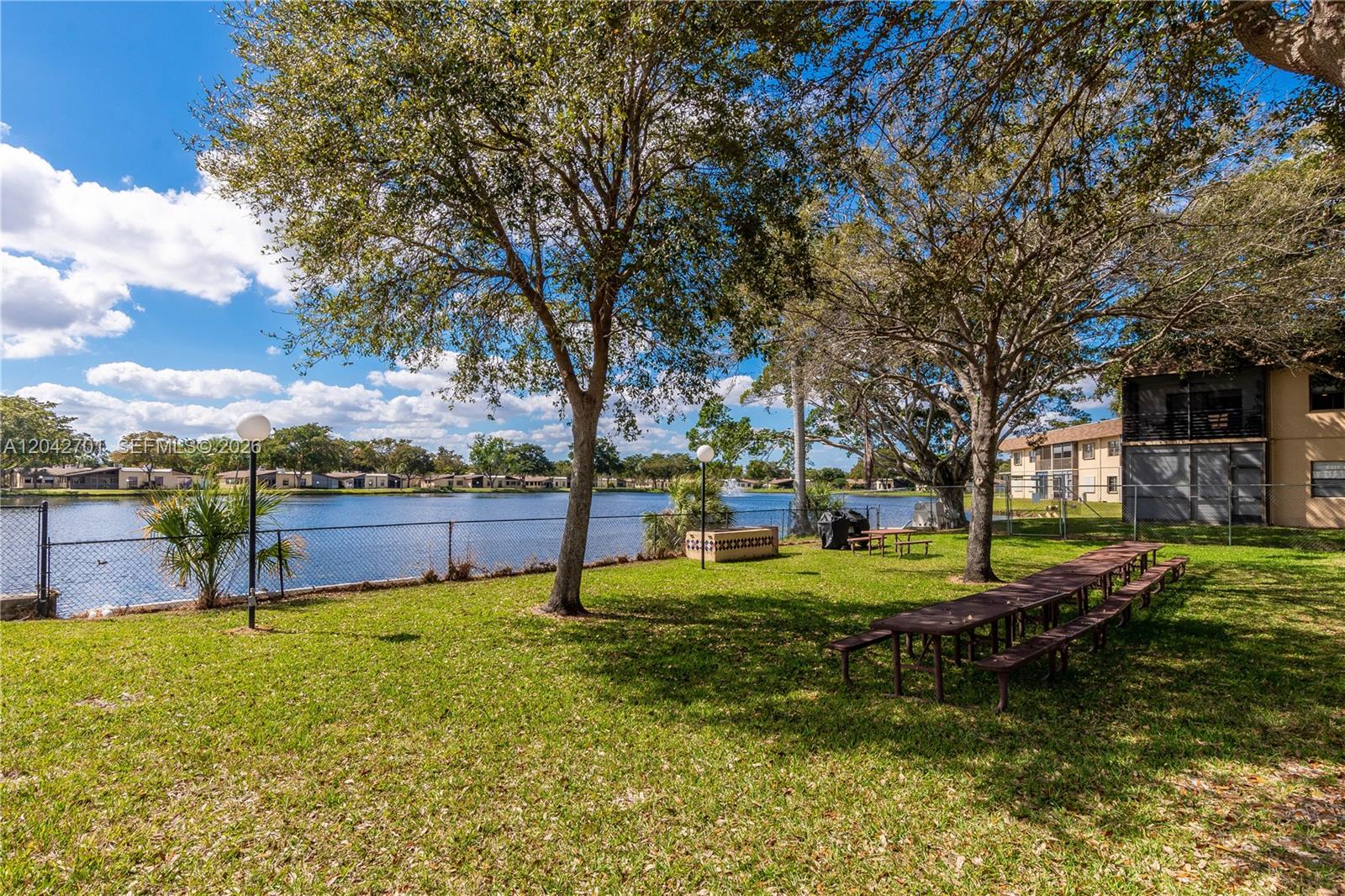 A grassy park area features picnic tables, mature trees, and a lake with a fountain — 300 Berkley Rd # 103, Hollywood FL 33024, HOLLYWOOD, FL