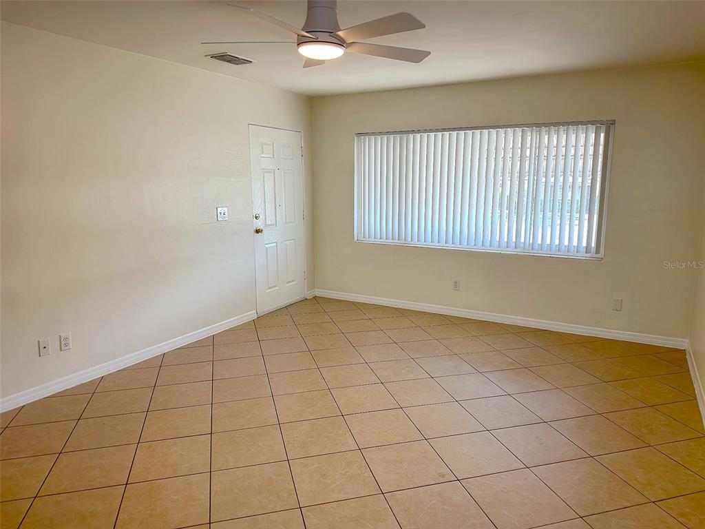 An empty room features beige tile flooring, a ceiling fan, and a large window with blinds — 1432 LOTUS PATH, CLEARWATER, FL