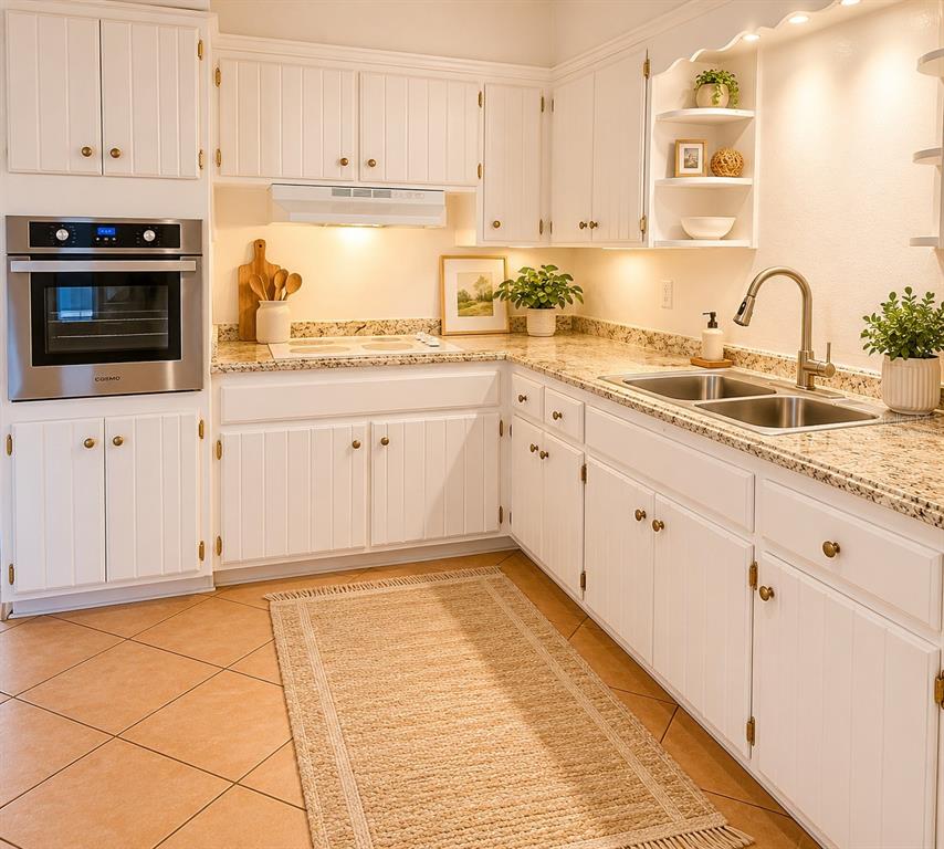 A kitchen with white cabinets, granite countertops, stainless steel oven, and light-colored tile flooring — 1432 LOTUS PATH, CLEARWATER, FL