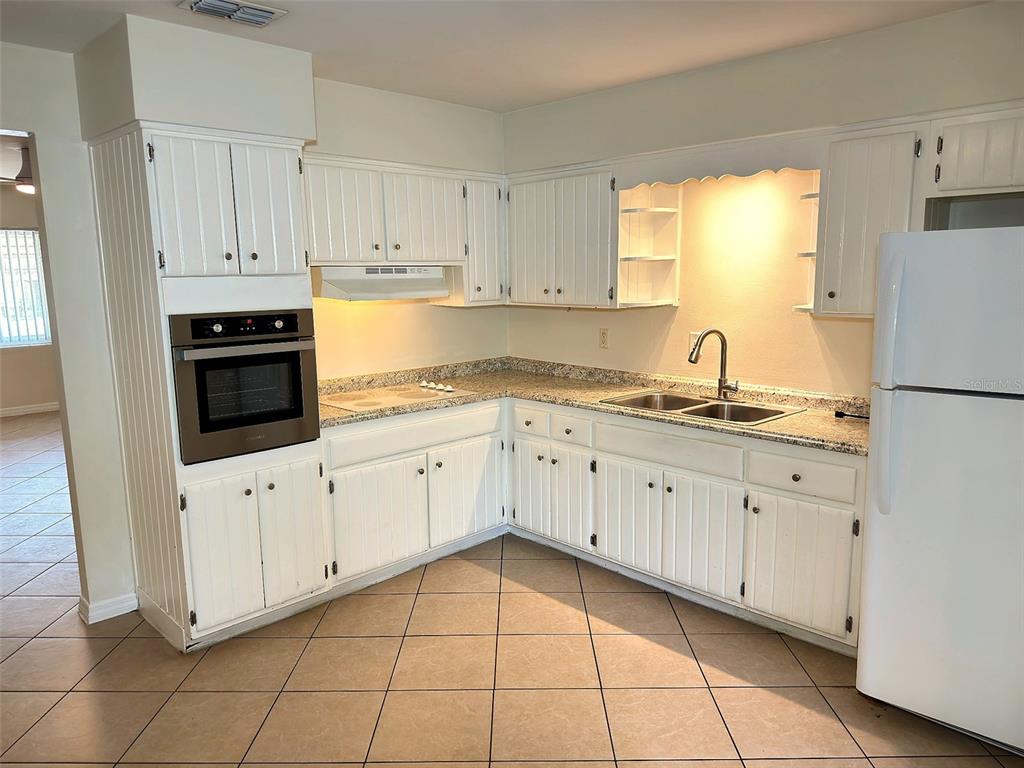 A kitchen features white beadboard cabinetry, granite countertops, a wall oven, and tile flooring — 1432 LOTUS PATH, CLEARWATER, FL