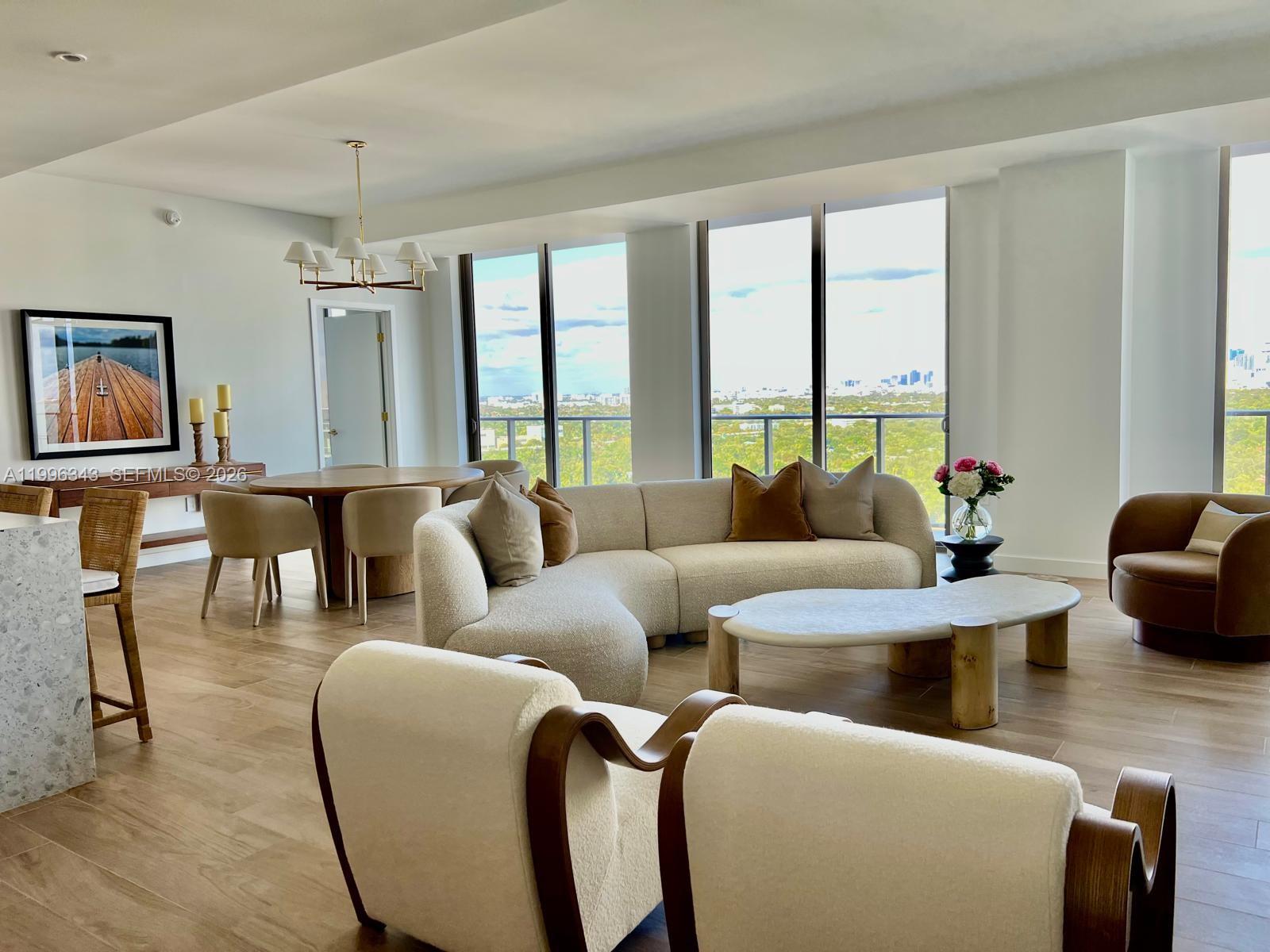 A bright, modern living and dining area features a curved sofa, wood flooring, and floor-to-ceiling windows — 2678 Tigertail Ave # 2006, Coconut Grove FL 33133, COCONUT GROVE, FL