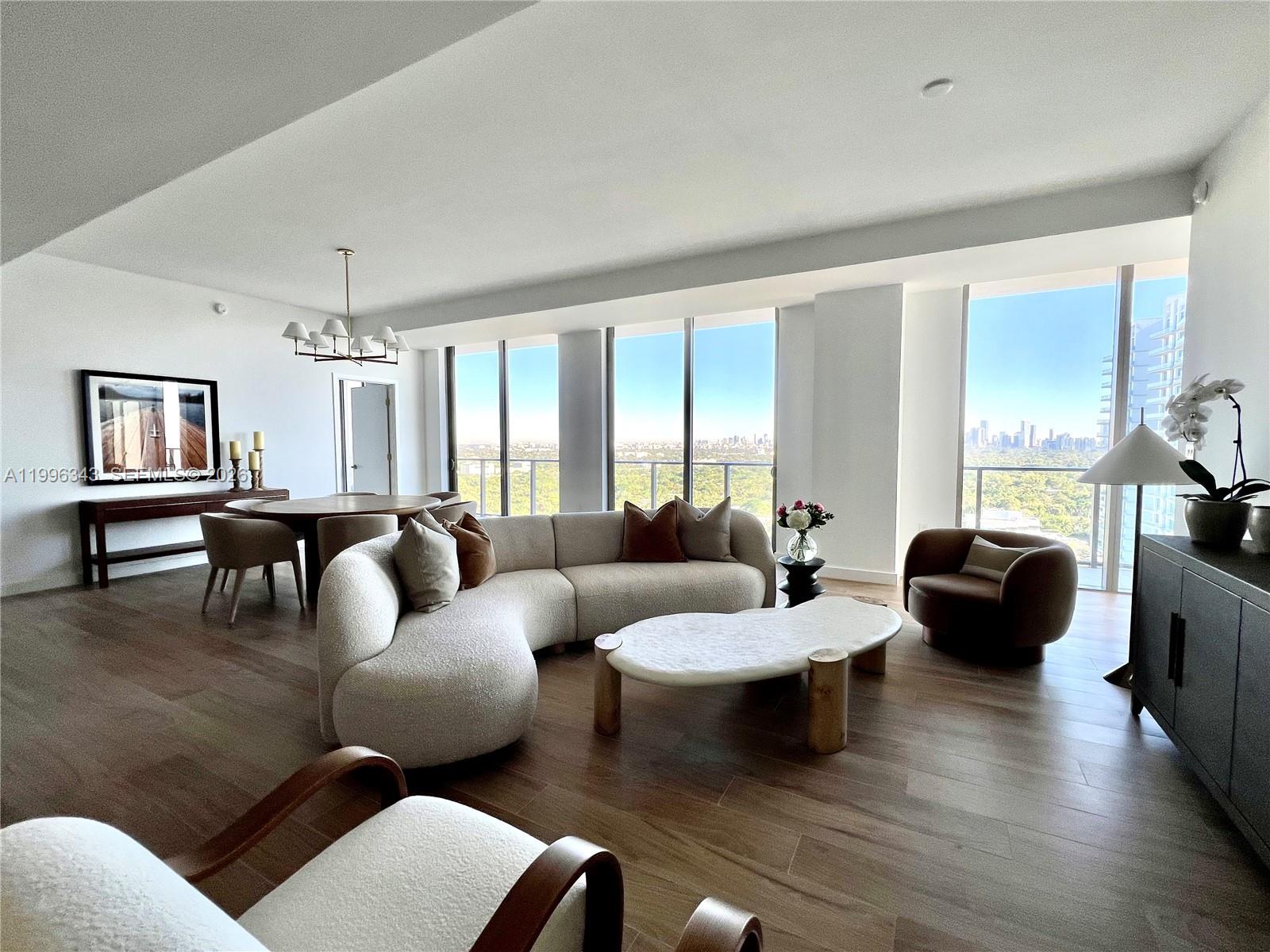 A modern living and dining area features a curved sofa, floor-to-ceiling windows, and city views — 2678 Tigertail Ave # 2006, Coconut Grove FL 33133, COCONUT GROVE, FL