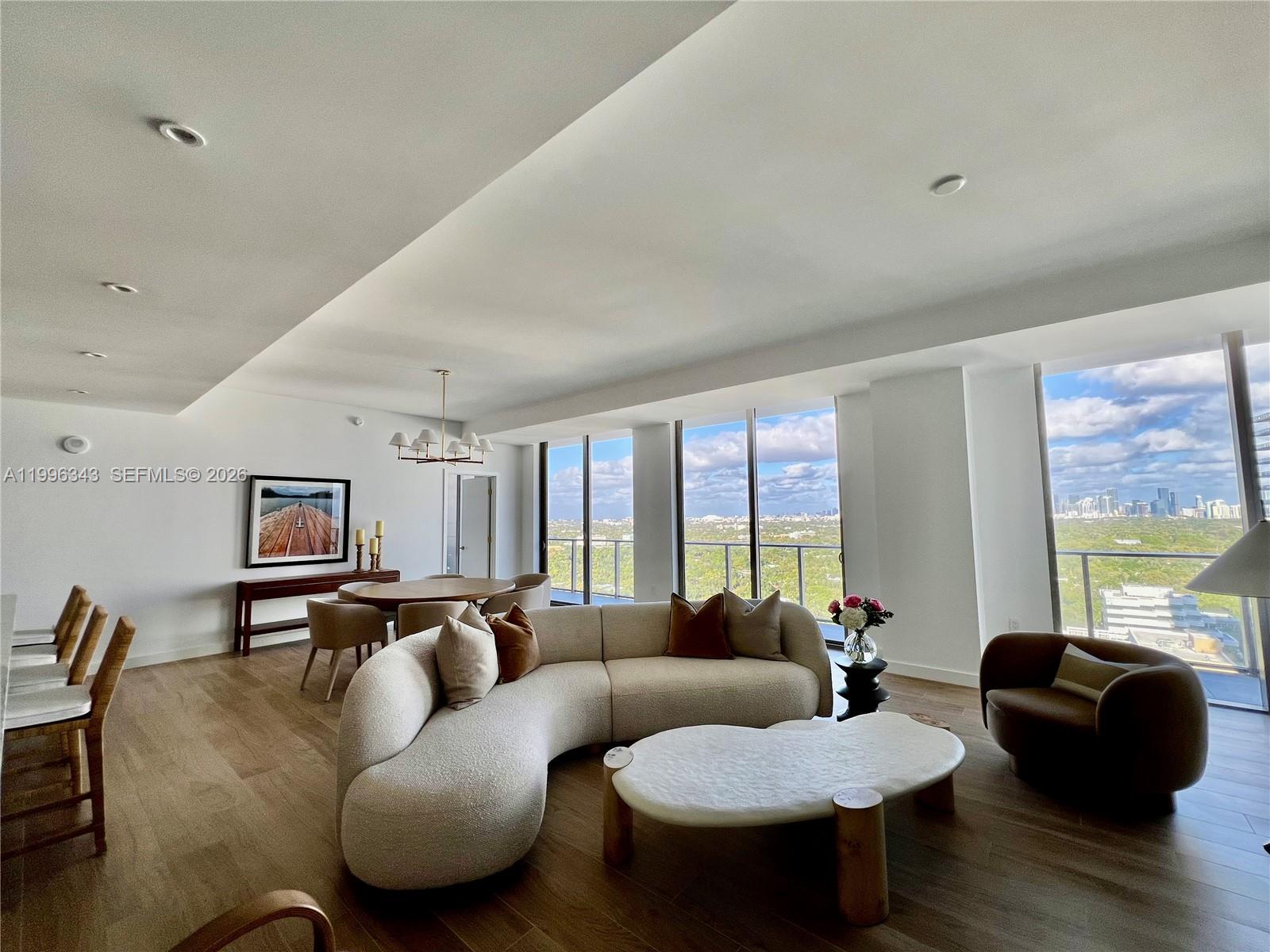 A modern living room features a curved sofa, coffee table, and floor-to-ceiling windows with views — 2678 Tigertail Ave # 2006, Coconut Grove FL 33133, COCONUT GROVE, FL