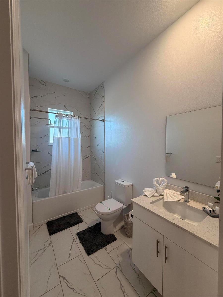 A bathroom features a white vanity, a toilet, and a bathtub with marble-patterned tile walls — 657 Trikomo Drive, Davenport FL 33896, DAVENPORT, FL