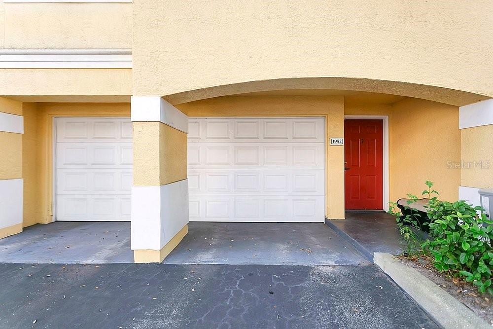 A two-car garage with white doors and a red front door under a covered entryway — 1952 LEGACY COVE DRIVE UNIT 1952, MAITLAND, FL