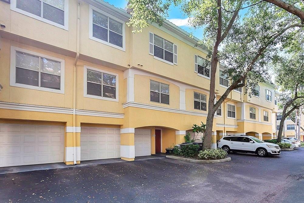 A three-story yellow townhouse complex features multiple garage doors and a white SUV parked outside — 1952 LEGACY COVE DRIVE UNIT 1952, MAITLAND, FL