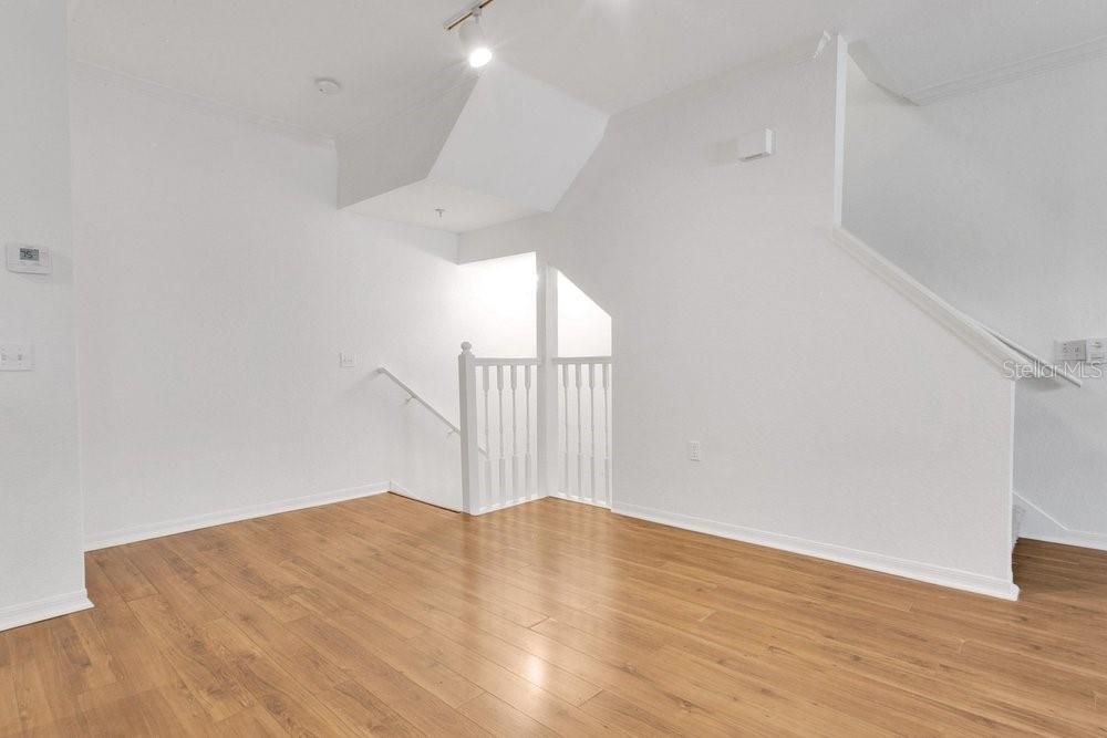 An empty room with light wood flooring, white walls, and a staircase with white railings — 1952 LEGACY COVE DRIVE UNIT 1952, MAITLAND, FL