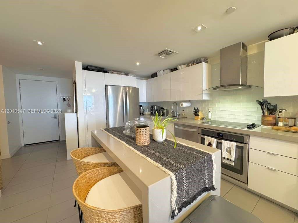 A modern kitchen features white glossy cabinetry, stainless steel appliances, and a central island — 1600 NE 1st Ave # 3312, Miami FL 33132, MIAMI, FL