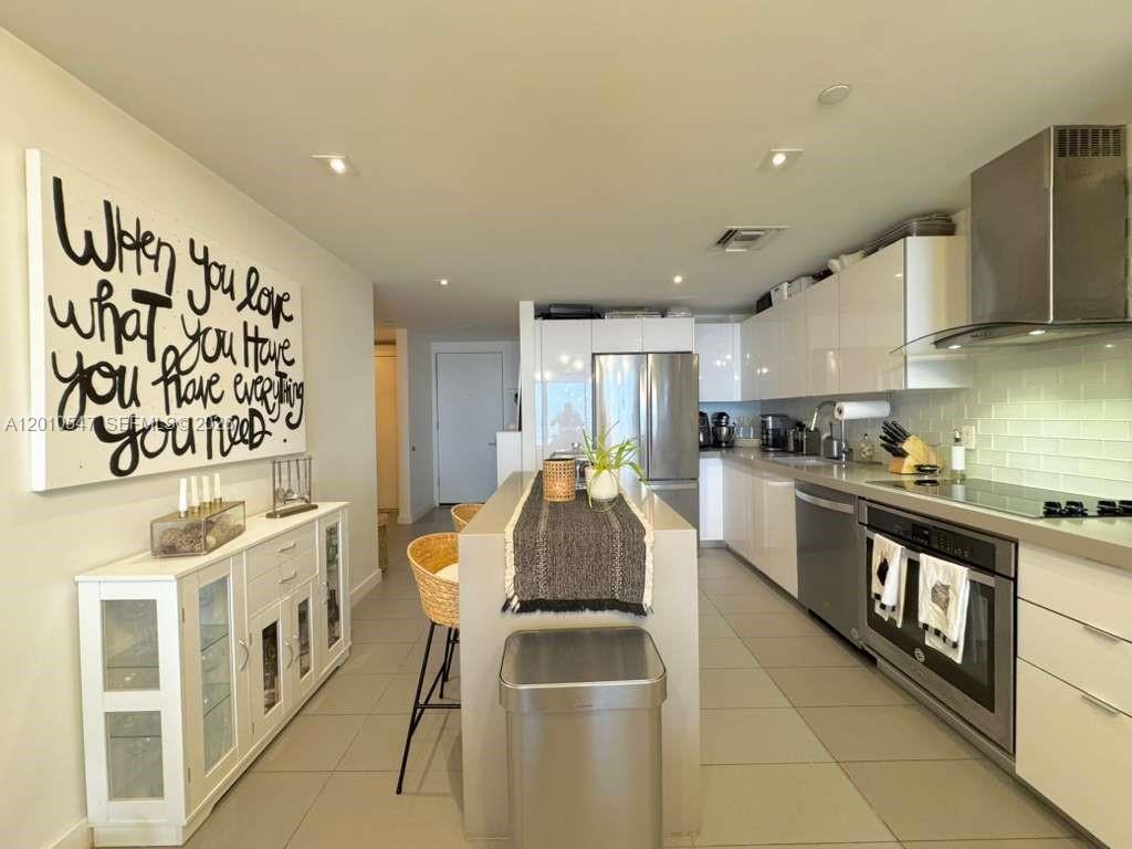 A modern kitchen features white cabinetry, stainless steel appliances, a central island, and wall art — 1600 NE 1st Ave # 3312, Miami FL 33132, MIAMI, FL