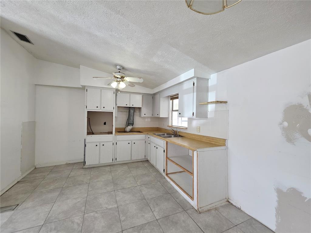 An unfinished kitchen features white cabinets, laminate countertops, gray tile flooring, and a ceiling fan — 4037 LAS VEGAS DRIVE, NEW PORT RICHEY, FL