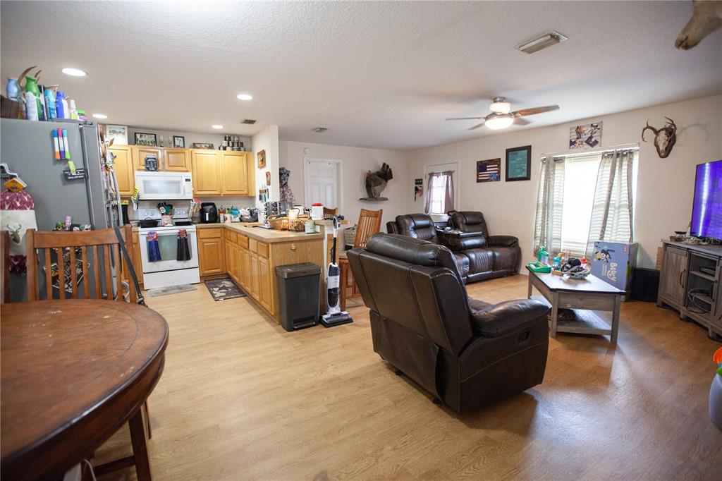 An open-concept kitchen and living area features light wood cabinets, laminate flooring, and leather recliners — 3554 COUNTY ROAD 230C, WILDWOOD, FL