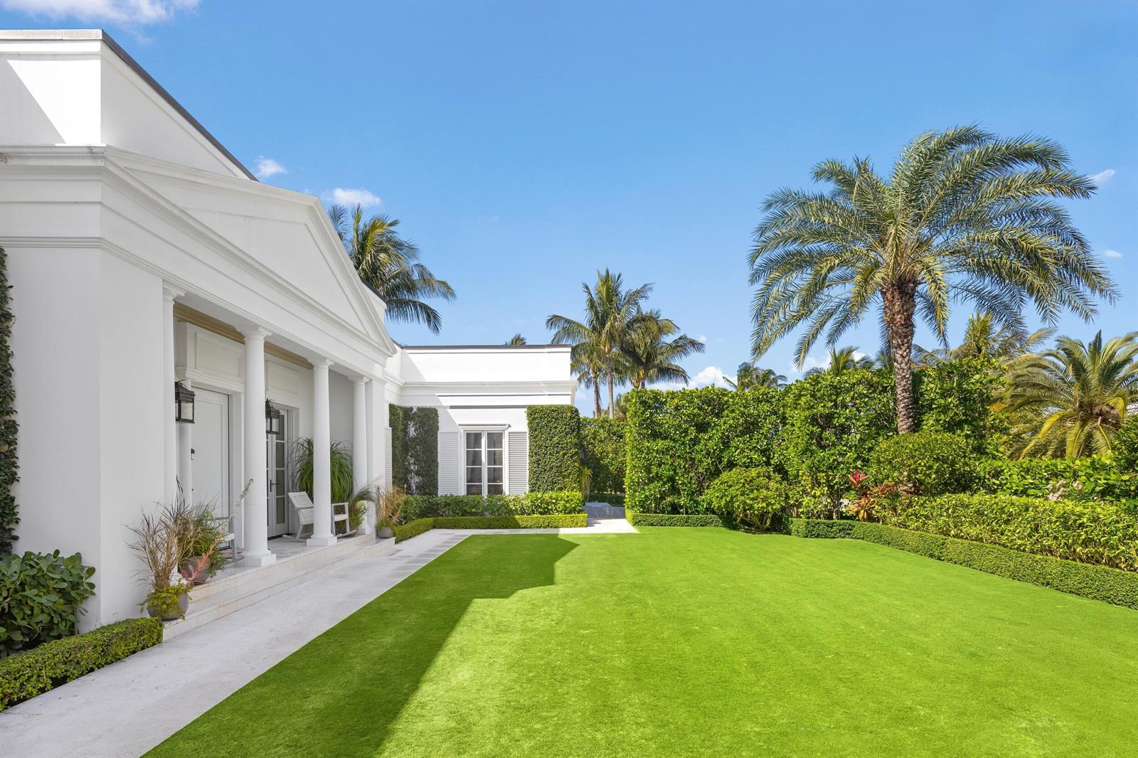 A white neoclassical house features a columned porch overlooking a manicured lawn and palm trees — 208 Sandpiper Drive, Palm Beach FL 33480, PALM BEACH, FL