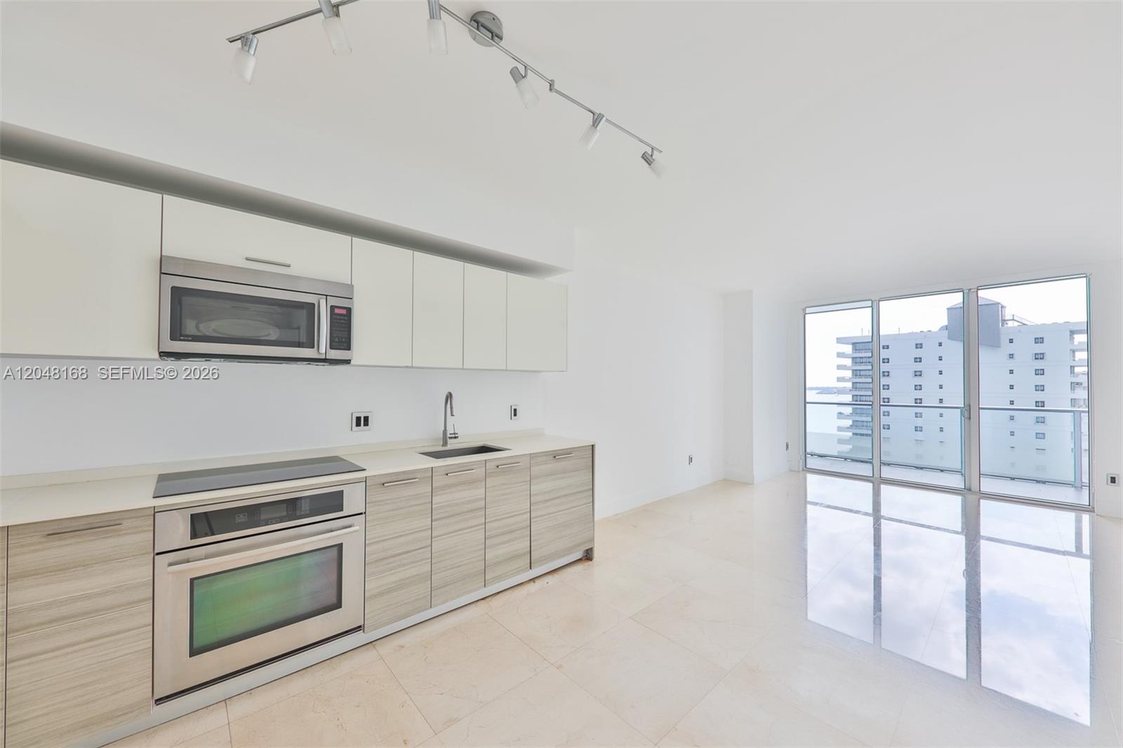 A modern kitchen with light wood cabinets and stainless steel appliances opens to a balcony — 1300 Brickell Bay Dr # 1206, Miami FL 33131, MIAMI, FL