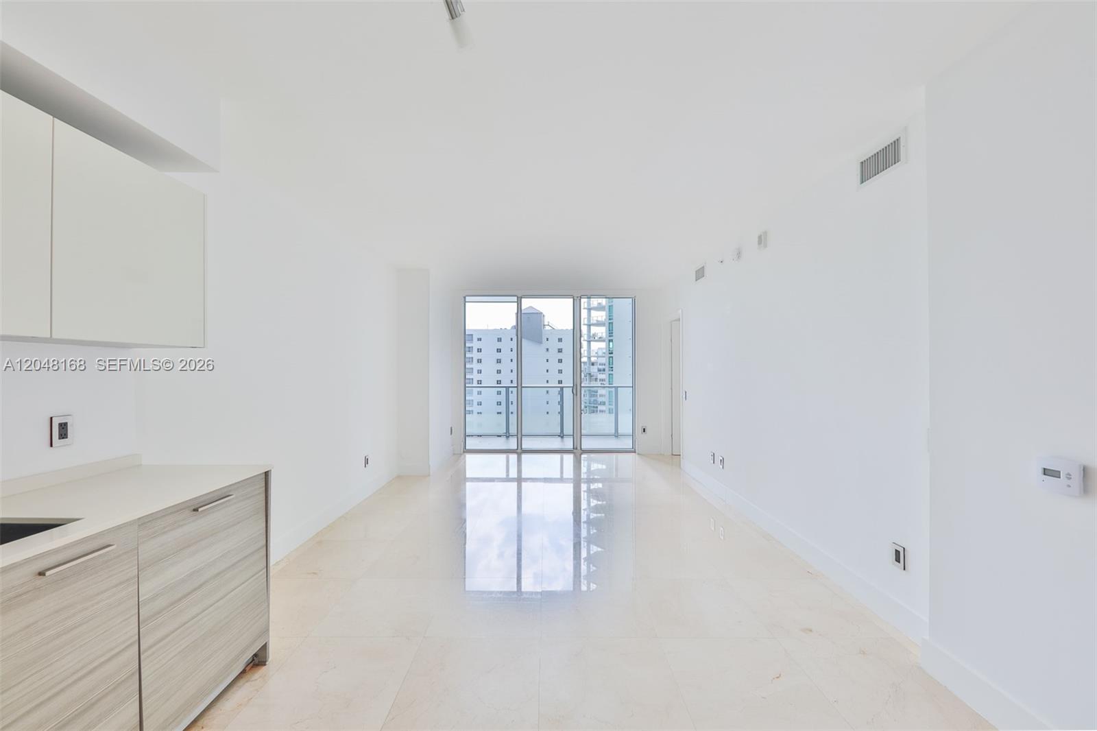 A bright, empty room features white walls, light tile flooring, and a glass balcony door — 1300 Brickell Bay Dr # 1206, Miami FL 33131, MIAMI, FL