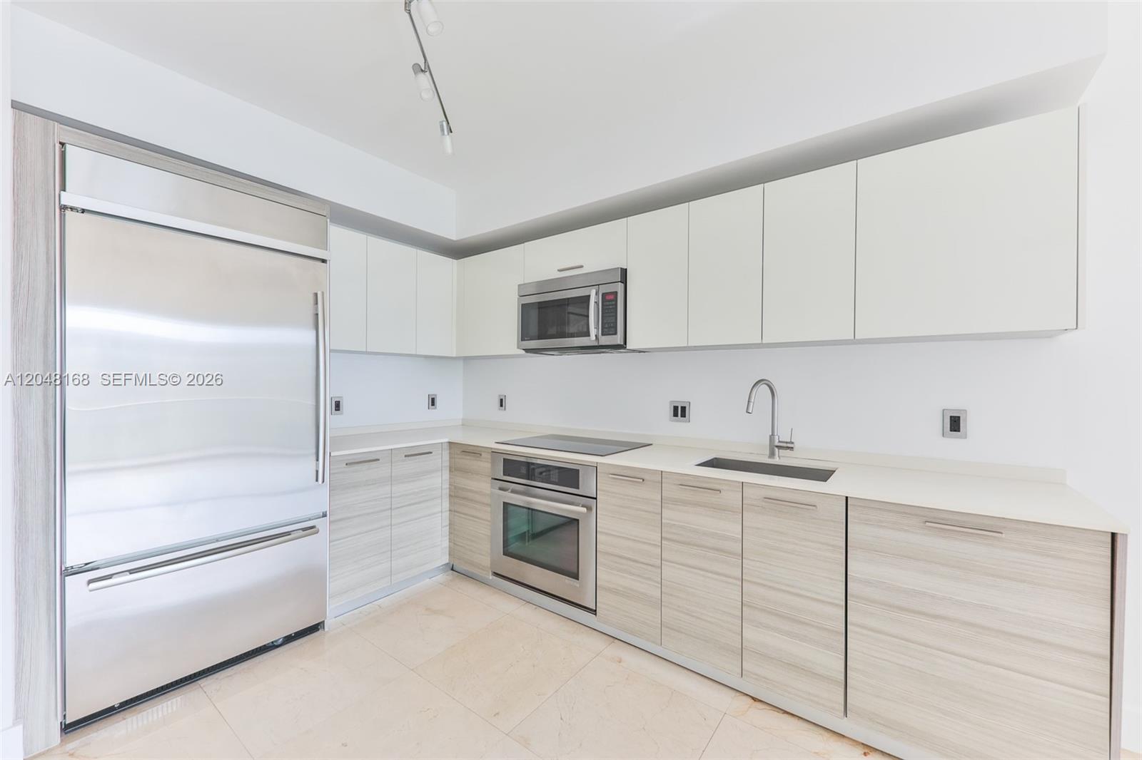 A modern kitchen features light wood-grain lower cabinets, white upper cabinets, and stainless steel appliances — 1300 Brickell Bay Dr # 1206, Miami FL 33131, MIAMI, FL