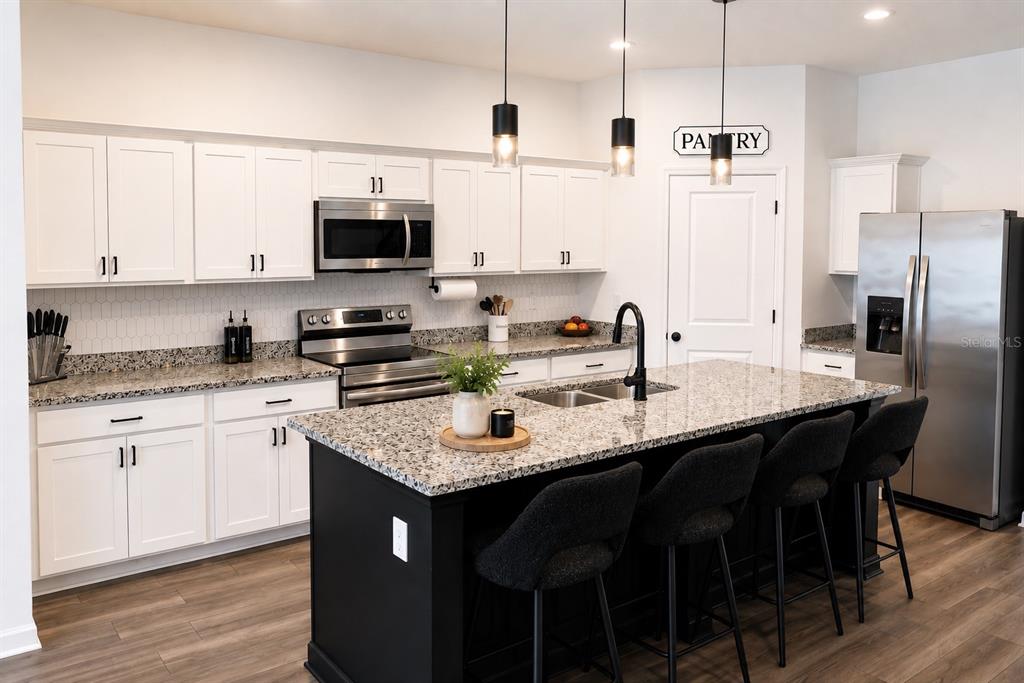 A kitchen features white cabinets, granite countertops, a black island with barstools, and stainless appliances — 35584 EASTBROOK AVENUE, ZEPHYRHILLS, FL