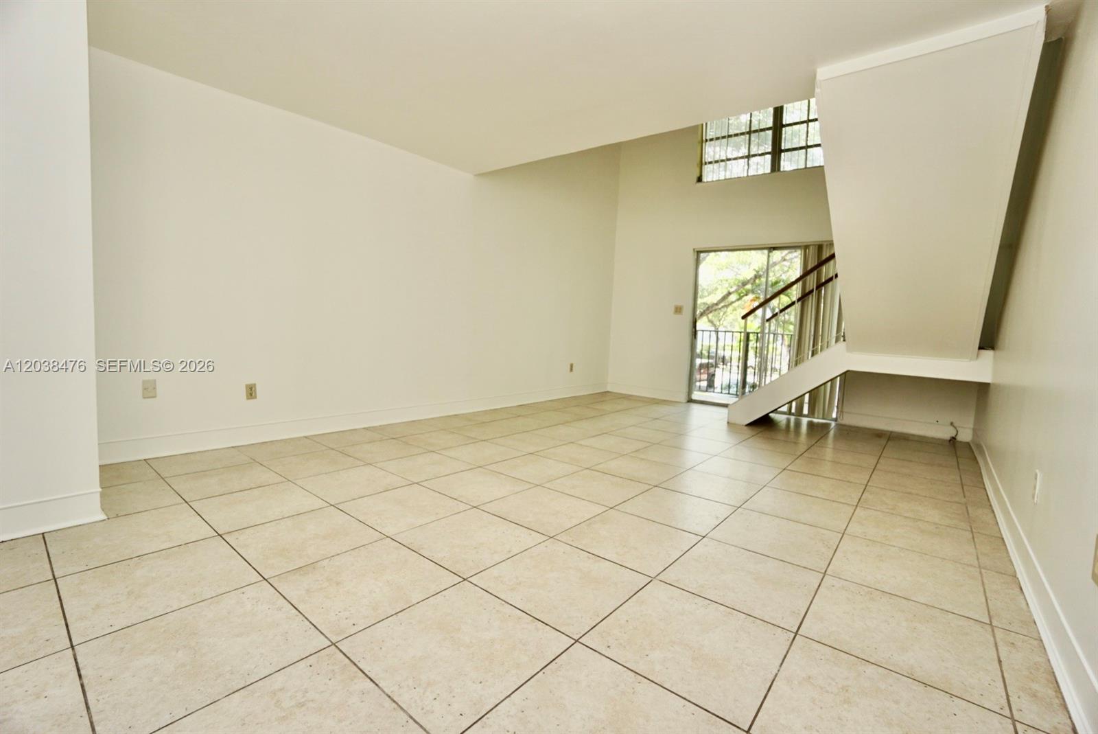 An empty living room features beige tile flooring, a staircase, and a sliding glass door — 8500 SW 109th Ave # 225, Miami FL 33173, MIAMI, FL