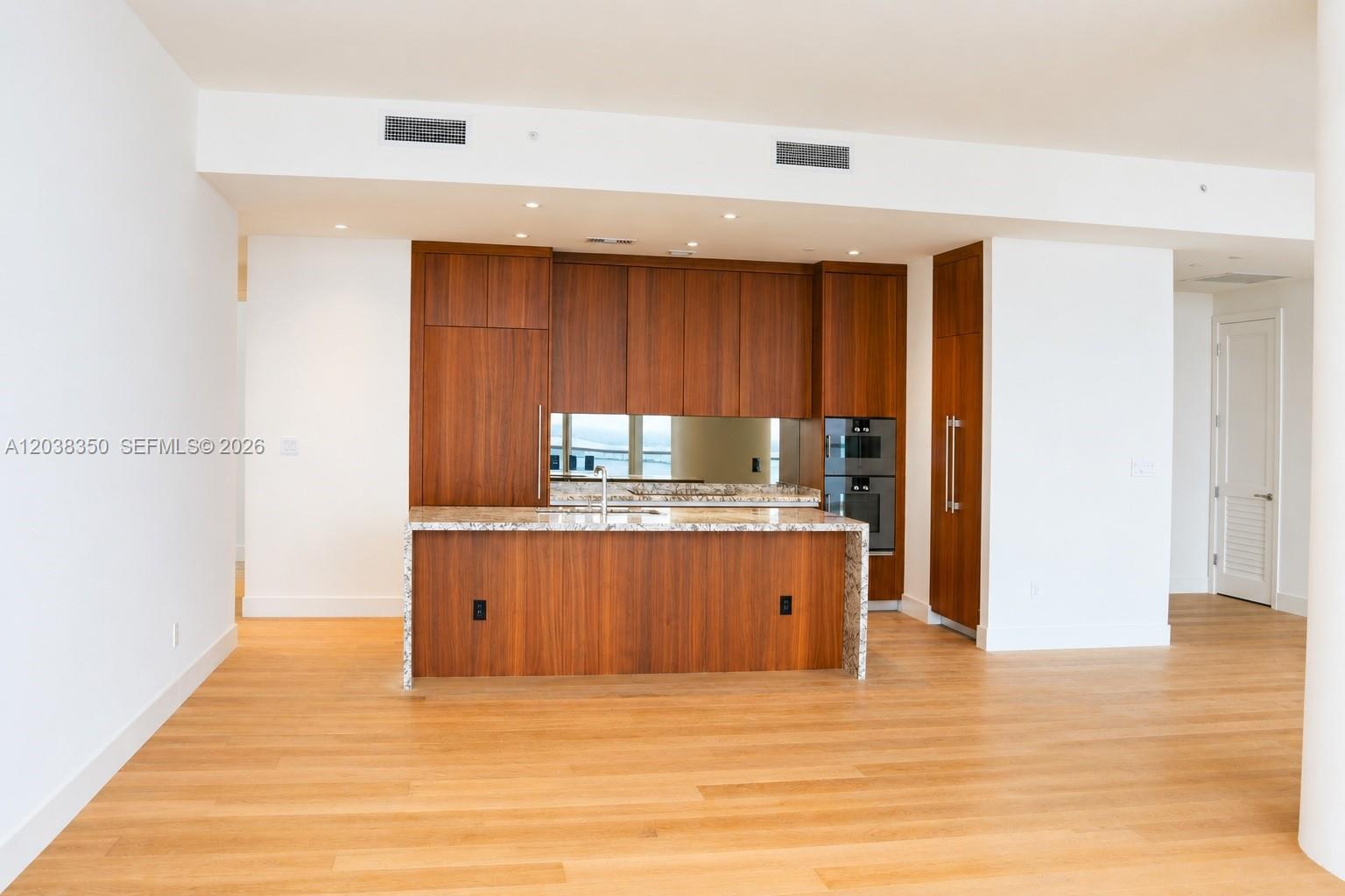 A modern kitchen features wood cabinetry, a granite-topped island, and light hardwood flooring — 175 SE 25th Rd # 3103, Miami FL 33129, MIAMI, FL