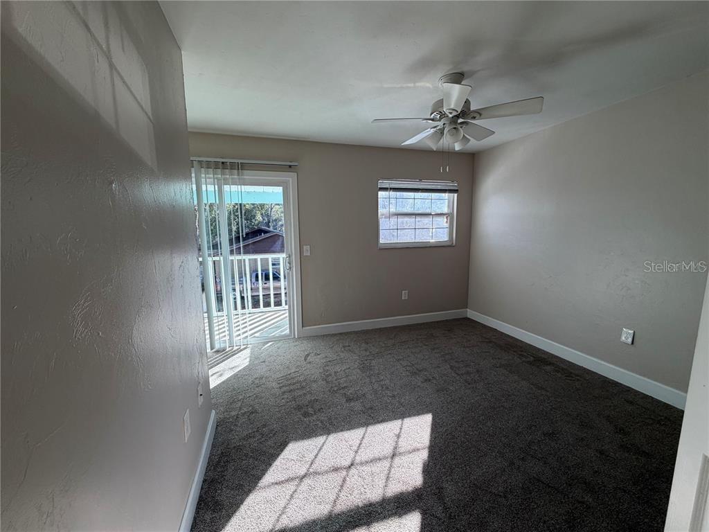 An empty bedroom features gray carpet, beige walls, a ceiling fan, and a sliding glass door — 1718 SW 69 TERRACE, GAINESVILLE, FL