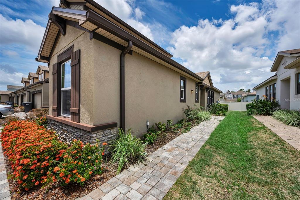 The exterior side view of a tan stucco house features a stone base and walkway — 11823 BROOKSIDE DRIVE, BRADENTON, FL