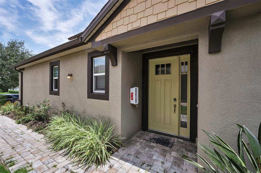 The exterior of a home features a light green front door, stucco walls, and pavers — 11823 BROOKSIDE DRIVE, BRADENTON, FL