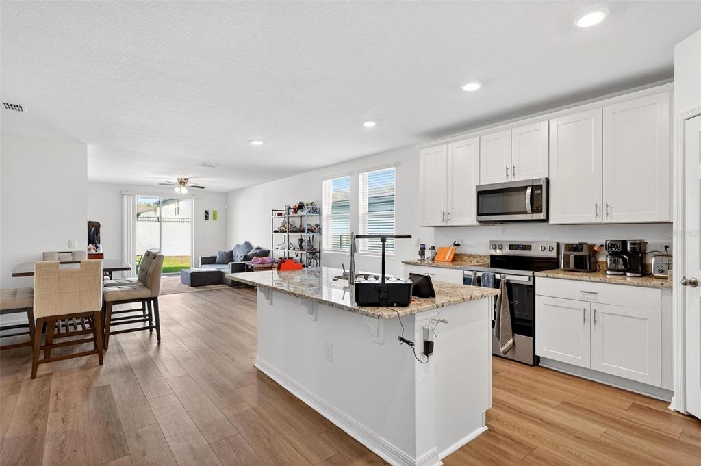 A kitchen with white cabinets, granite countertops, and stainless steel appliances opens to a living area — 2514 MOOSE TRAIL PLACE, DAVENPORT, FL