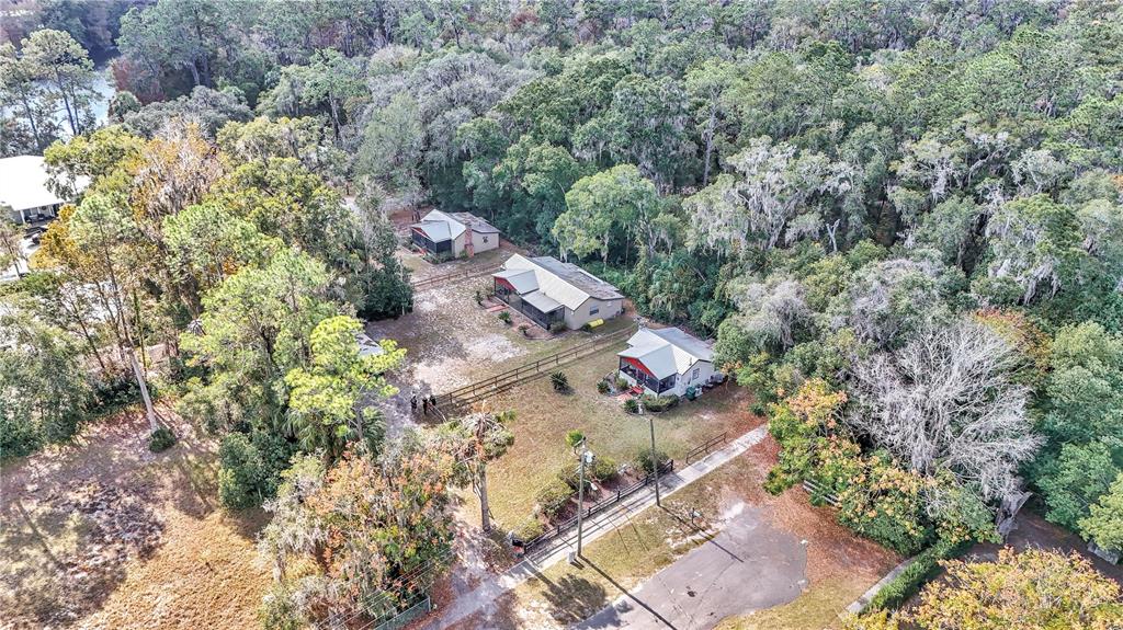 An aerial view shows three houses situated on a wooded lot with a paved driveway — 20990 W PENNSYLVANIA AVENUE, DUNNELLON, FL
